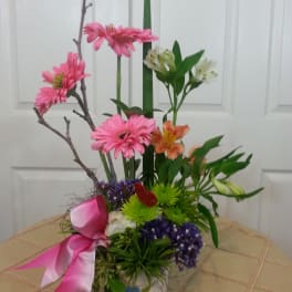 Pink and orange mixed flower arrangement in a decorated vase with a pink ribbon