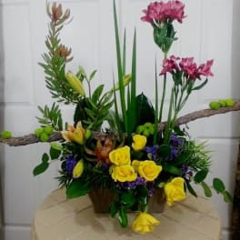 Tall floral arrangement with yellow roses and pink lilies in a container