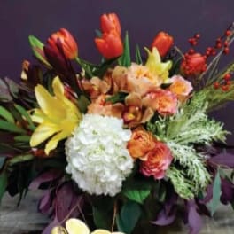 Low arrangement of orange tulips, yellow lilies, white hydrangea, and roses in a container