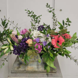 Mixed floral arrangement with roses, lilies, and gerbera daisies in a metal container