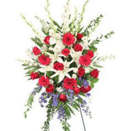 Tall standing spray of red roses and gerbera daisies with white lilies and purple accents on an easel.