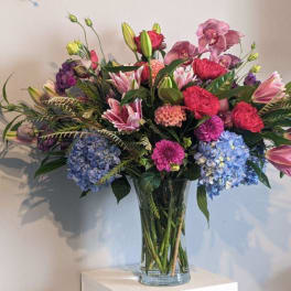 Mixed bouquet of pink, purple, and blue flowers in a clear glass vase