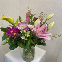 Mixed bouquet of pink lilies and purple flowers in a glass vase