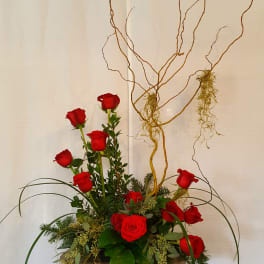 Tall red rose arrangement with curly branches in a silver vase