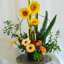 Tall floral arrangement with sunflowers, orange roses, and yellow daisies in a basket