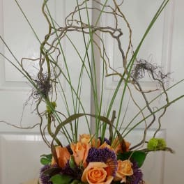 Orange roses with purple blooms in a low green container and tall curly branches
