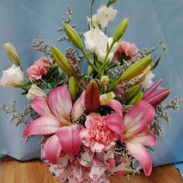 Pink lilies and carnations arranged with white blooms in a ribboned bouquet
