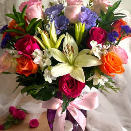 Mixed bouquet of roses and lilies in a purple vase with a pink ribbon