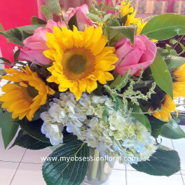 Bouquet of sunflowers, pink roses, and pale hydrangeas in a glass vase