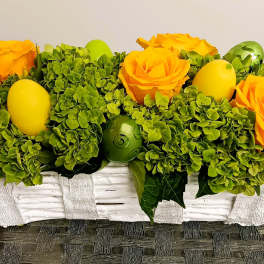 Yellow roses and green hydrangeas in a white basket with decorative eggs