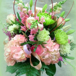 Pink and green mixed bouquet in a glass vase with ribbon loops