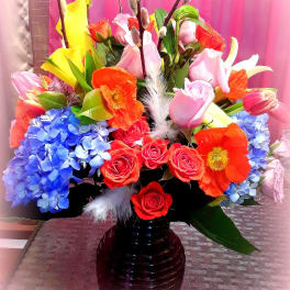Colorful bouquet of roses, tulips, calla lilies, and hydrangeas in a dark vase