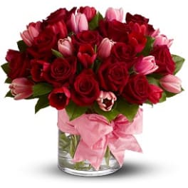 Red roses and pink tulips in a clear glass vase with a pink ribbon