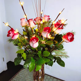 Tall vase arrangement of red and white roses with lit decorative branches