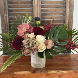 Tropical bouquet with orchids, roses, and dark dahlias in a white vase
