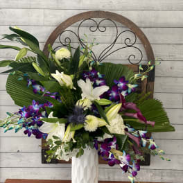 White lilies and purple orchids in a tall white vase