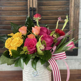 Colorful rose arrangement in a white ceramic vase with a striped ribbon
