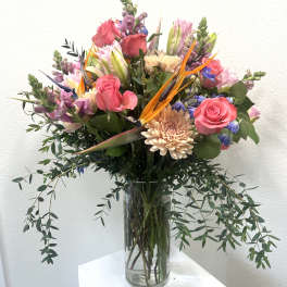 Mixed bouquet of pink roses, lilies, and orange bird of paradise in a glass vase
