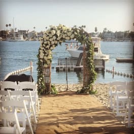 White floral arch on a beach aisle with chairs facing the water