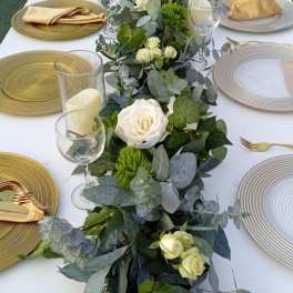 Long table centerpiece with white roses and greenery on a set dining table