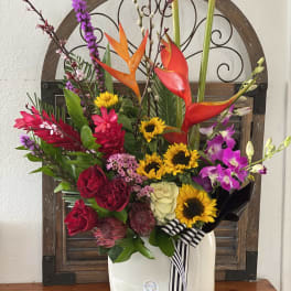 Colorful tropical flower arrangement in a white vase with a striped ribbon