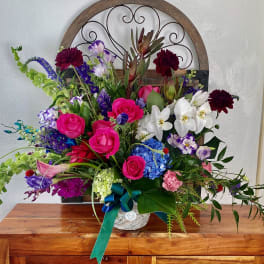 Colorful mixed flower arrangement in a white container with a teal ribbon
