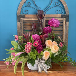 Mixed pink and peach floral arrangement in a white container with a striped ribbon