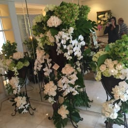 Tall white floral arrangements on black stands in a room