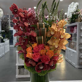 Tall arrangement of orchids and roses in a green glass vase