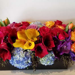 Colorful floral arrangement with roses, calla lilies, and hydrangeas in a black container