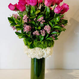 Pink roses in a tall glass vase with white and green accents