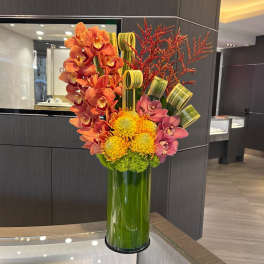 Orange and pink orchids with yellow blooms in a tall green vase