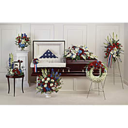 Patriotic red, white, and blue funeral floral set around an open casket with a folded flag