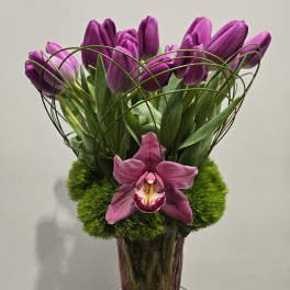 Purple tulips and an orchid in a glass vase with green moss
