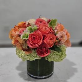 Pink and orange rose arrangement in a dark glass vase