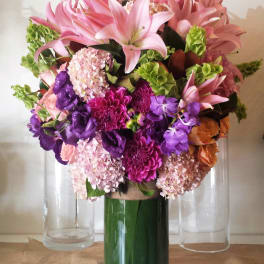 Pink lilies and purple flowers arranged in a tall glass vase