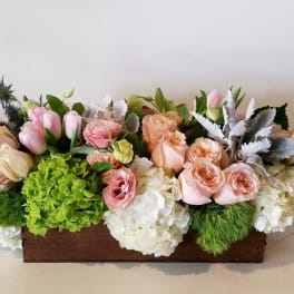 Low floral arrangement in a wooden box with pink and peach roses