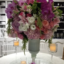Large pink and purple floral arrangement in a tall vase on a table