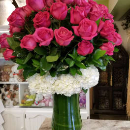 Pink roses arranged above white hydrangeas in a green glass vase