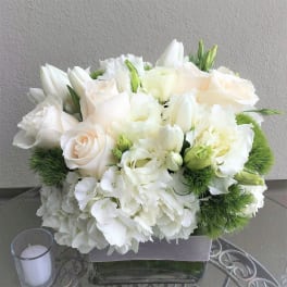 White floral arrangement in a square glass vase with a candle nearby