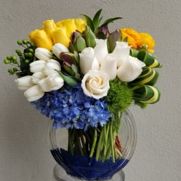 Bouquet of yellow, white, blue, and orange flowers in a clear glass vase