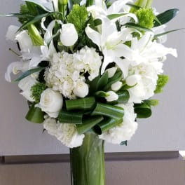 White lilies and roses arranged in a tall green glass vase