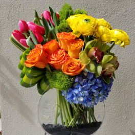 Colorful bouquet of tulips, roses, orchids, hydrangea, and yellow blooms in a glass vase