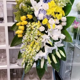 Large standing floral spray with white lilies, yellow roses, and blue hydrangeas