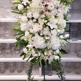 Large white funeral spray with lilies, roses, and orchids on a standing easel
