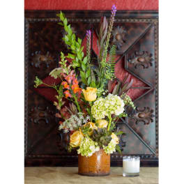 Tall floral arrangement in a brown vase with yellow roses and green hydrangeas