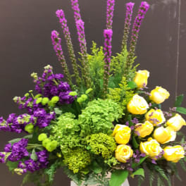 Yellow roses and purple flowers in a white pedestal vase