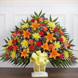 Large standing floral spray with orange lilies, yellow mums, and red roses