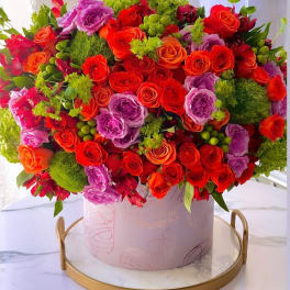 Large bouquet of red, orange, and purple roses in a pink round box