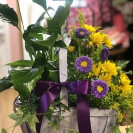 Yellow and purple flowers arranged in a wooden basket with a purple ribbon